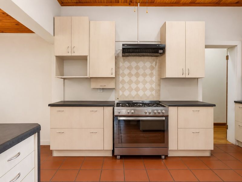 Functional kitchen featuring light wood-tone cabinetry, dark countertops, a stainless steel gas stove with extractor fan, and terracotta floor tiles.