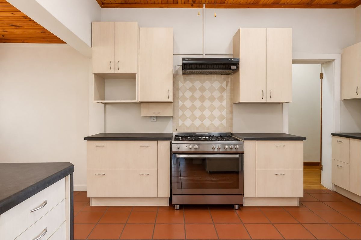 Functional kitchen featuring light wood-tone cabinetry, dark countertops, a stainless steel gas stove with extractor fan, and terracotta floor tiles.