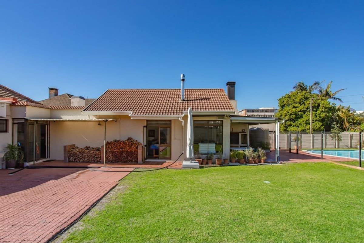 Rear view of the property featuring a tiled roof, paved patio area, and a well-maintained garden with access to a swimming pool.