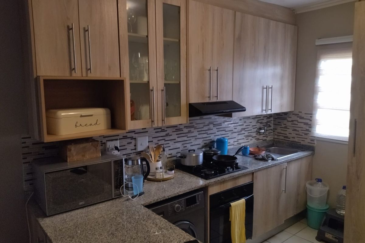 A functional kitchen featuring light wood-finish cabinetry, granite countertops, a mosaic tile backsplash, and integrated appliances including a gas hob and oven.