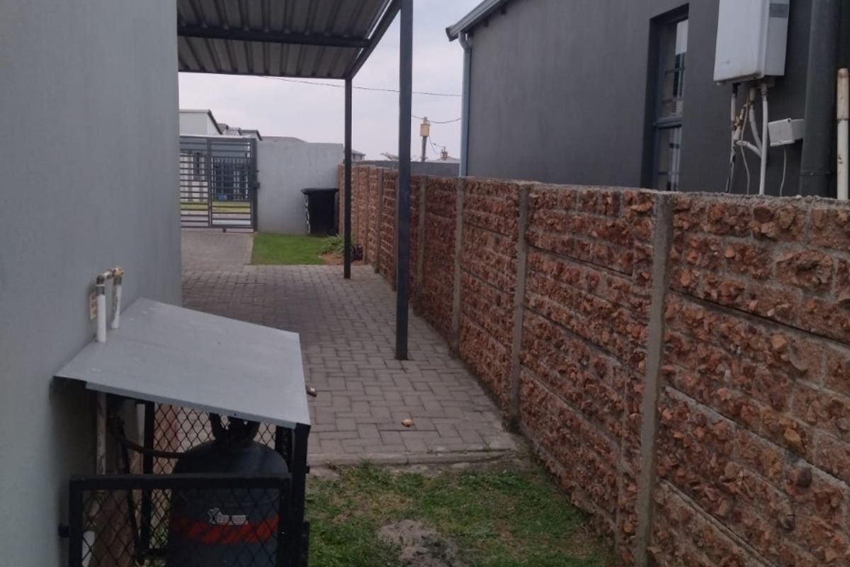 Side exterior area featuring a paved walkway, carport structure, gas geyser installation, and secure gas cylinder storage enclosure.