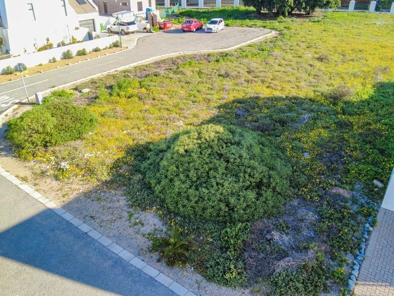An aerial view of a vacant residential plot featuring natural vegetation, adjacent paved driveway, and established kerbing in a residential estate setting.