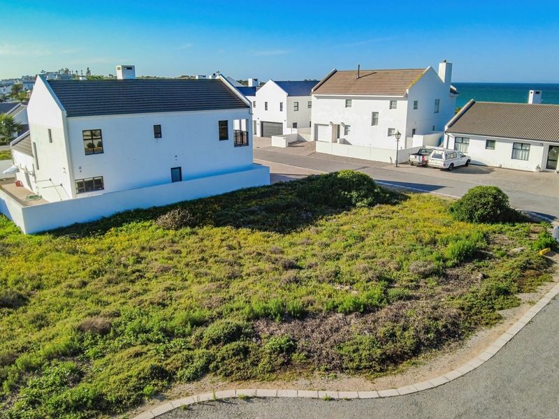 An aerial view of a vacant residential plot situated in a coastal neighborhood, featuring established road access and surrounding residential properties.