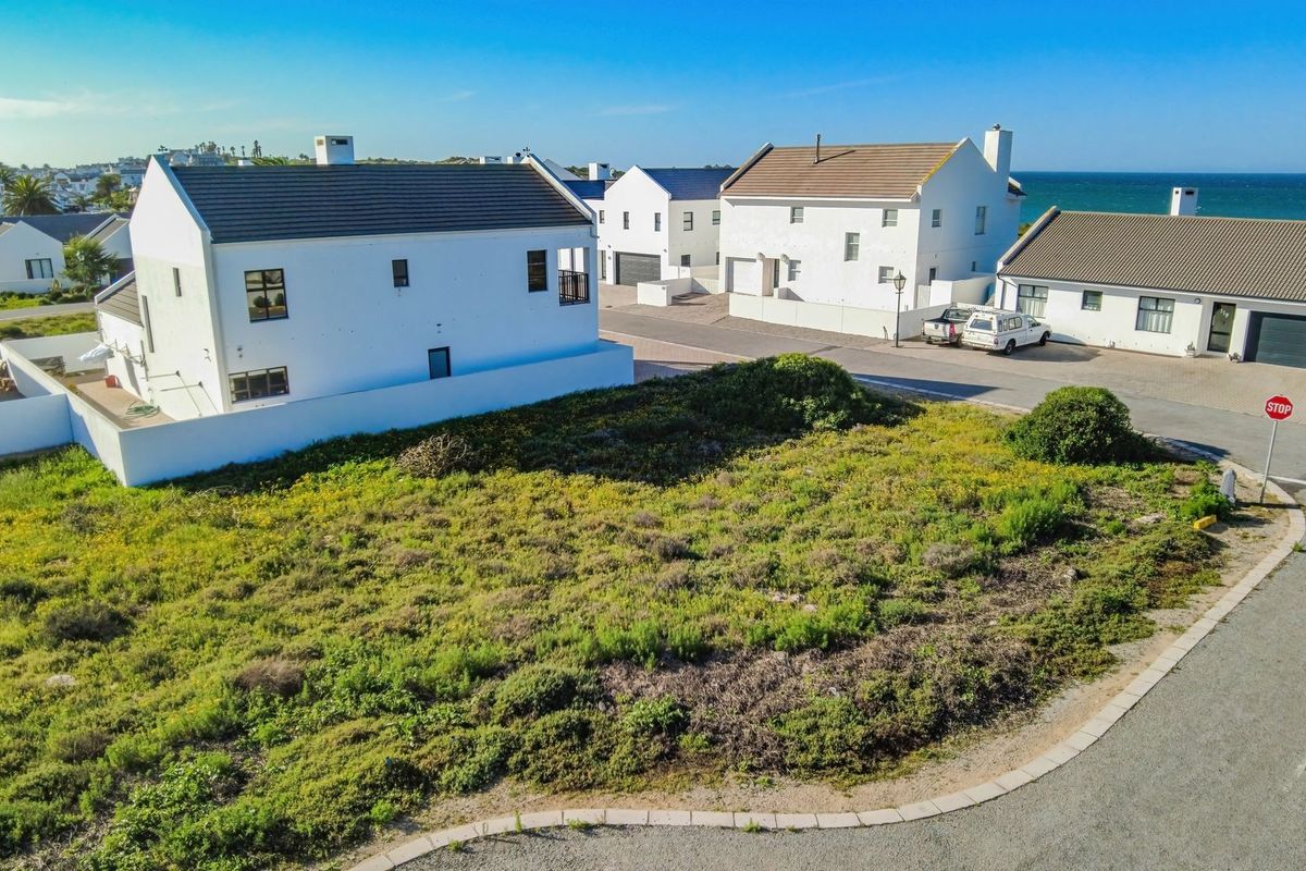 An aerial view of a vacant residential plot situated in a coastal neighborhood, featuring established road access and surrounding residential properties.