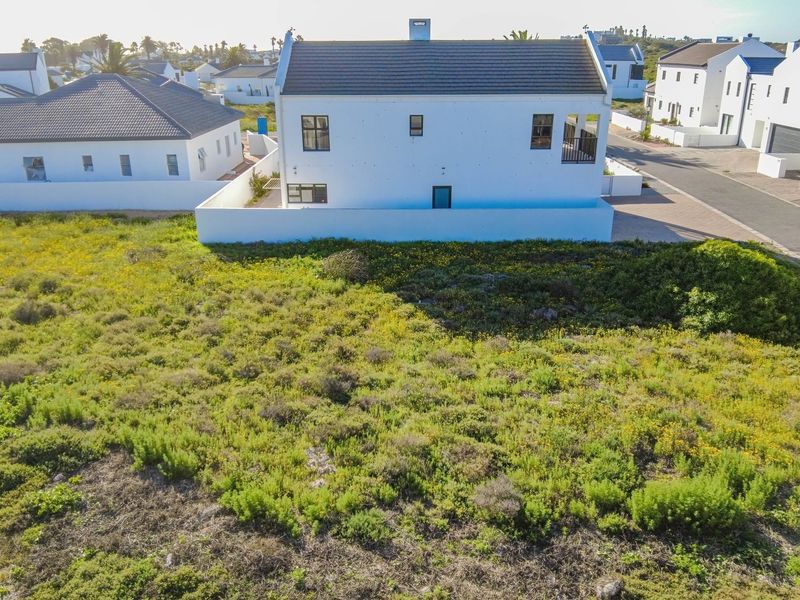 An aerial view of a vacant residential plot situated in a developed estate, featuring natural vegetation and adjacent to existing residential properties.