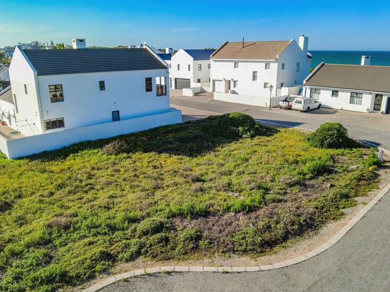 An aerial view of a vacant residential plot situated in a developed coastal neighborhood with paved street access.