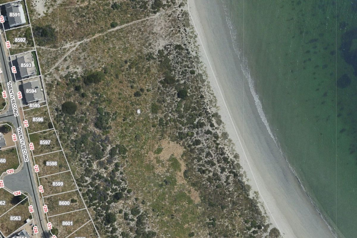 Aerial view of a vacant residential plot situated along the coastline, featuring direct beach access and proximity to established neighborhood infrastructure.