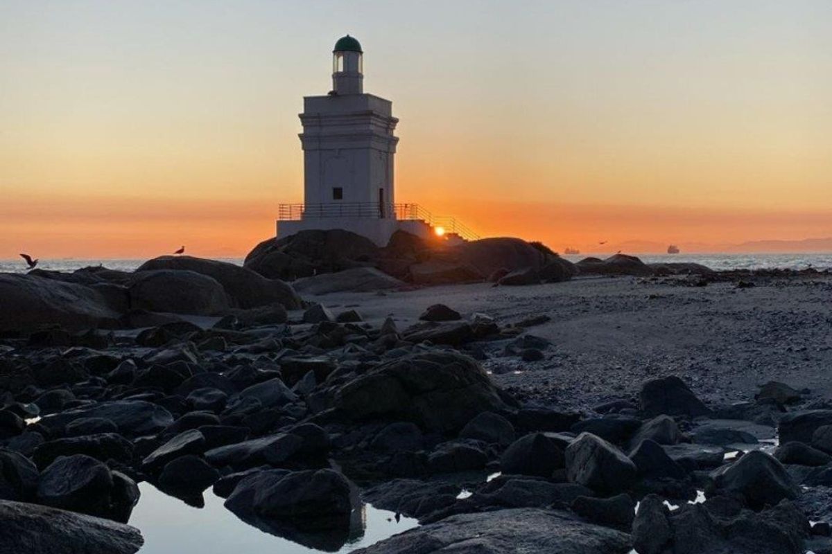 A scenic view of a lighthouse situated on a rocky coastal shoreline at sunset.