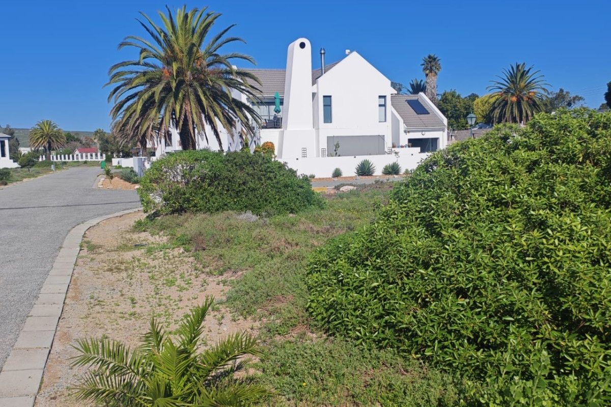 A view of a residential property from the street, featuring a white exterior facade, established landscaping, and a paved road.