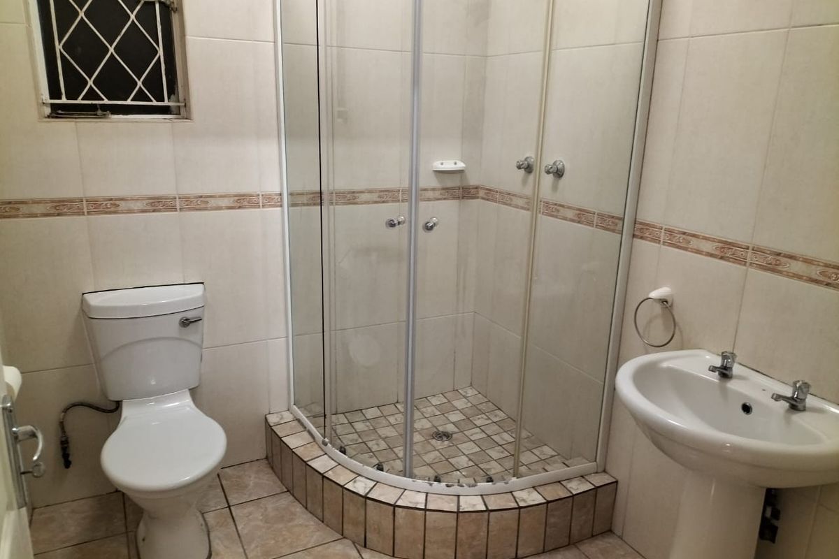 A functional bathroom featuring a corner shower enclosure, pedestal basin, and toilet with neutral wall tiling and tiled flooring.