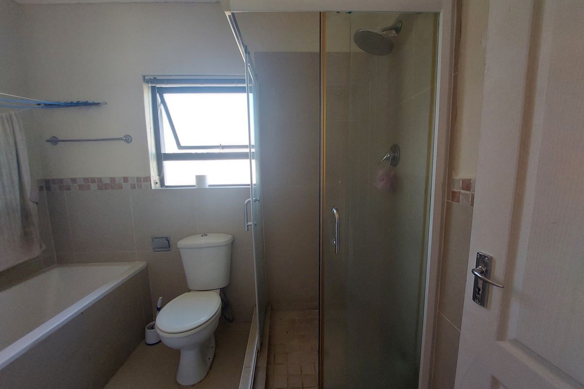 A functional bathroom featuring a separate bathtub, a glass-enclosed shower, and a standard toilet with neutral wall and floor tiling.