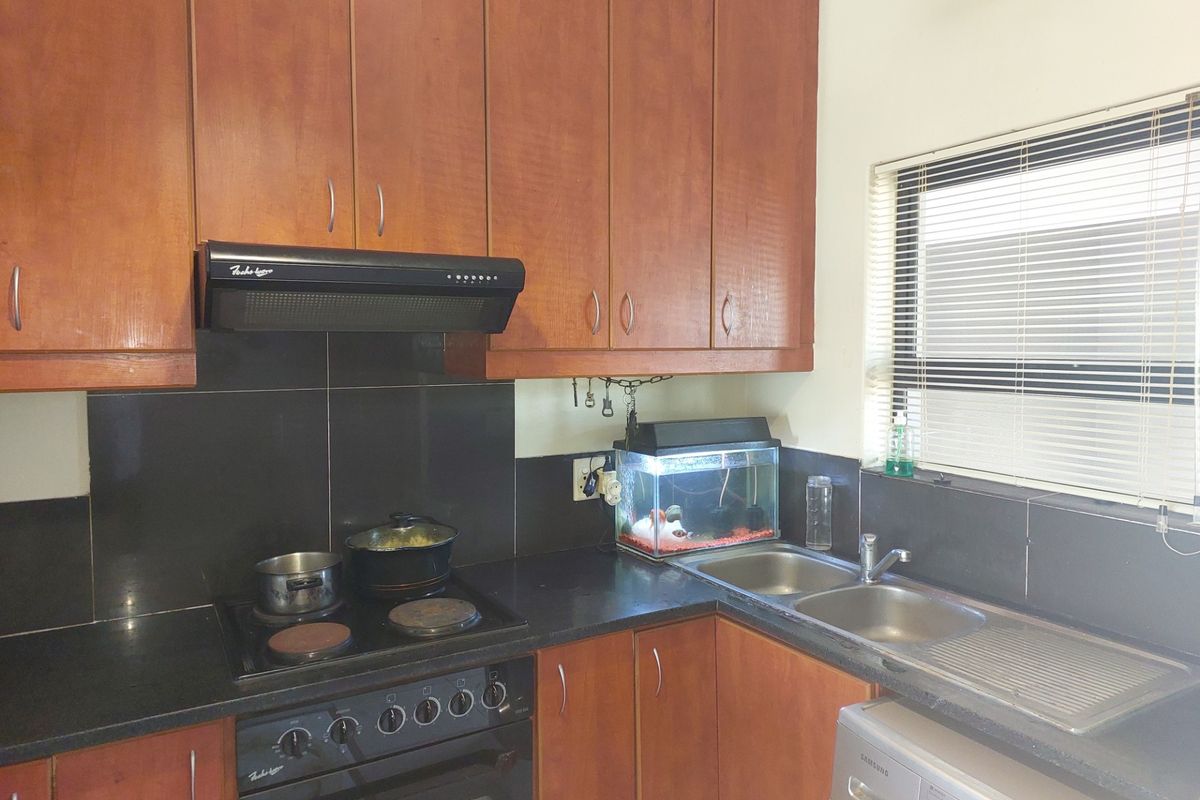 A functional kitchen featuring wooden cabinetry, black granite countertops, a tiled backsplash, and integrated appliances including an electric stove and double bowl sink.