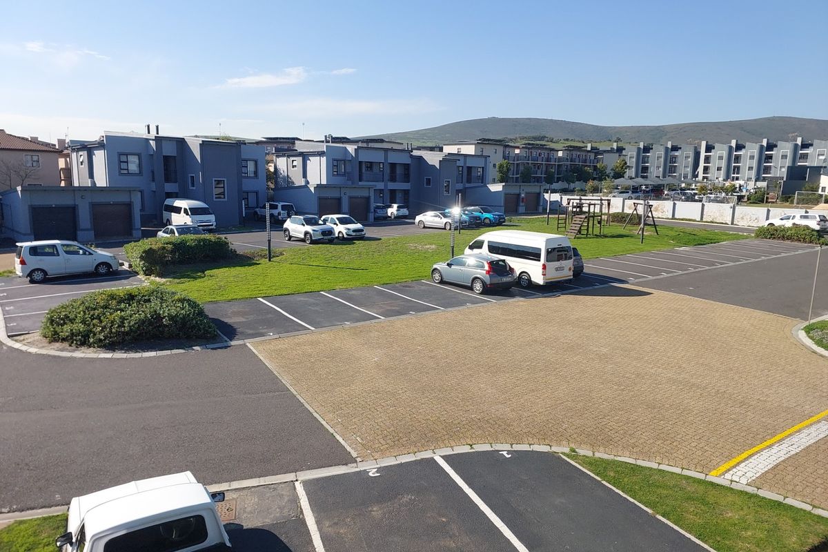 An elevated aerial view of the apartment complex grounds, featuring paved parking bays, communal green spaces, and a small playground area.
