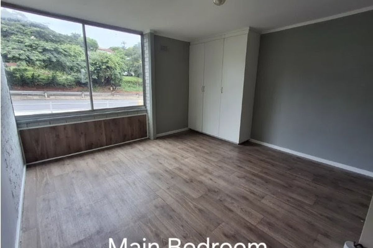 A spacious bedroom featuring wood-look laminate flooring, built-in wardrobes, and large windows providing natural light and an exterior view.