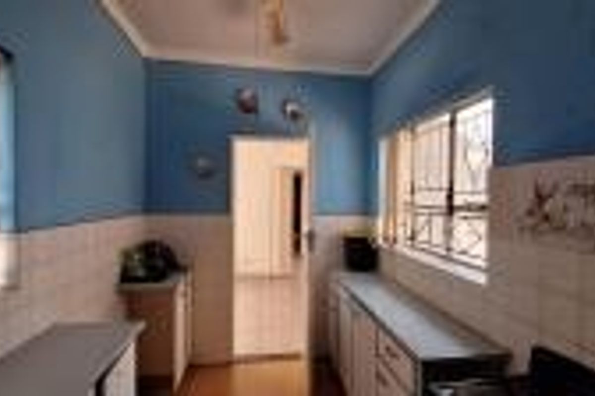 A functional kitchen space featuring built-in cabinetry, tiled splashbacks, and security bars on the windows, offering a practical layout for renovation.