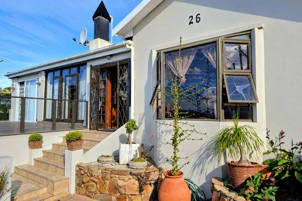 Exterior view of the home featuring a raised tiled patio, stone-clad garden bed, and a prominent bay window with a cracked pane.