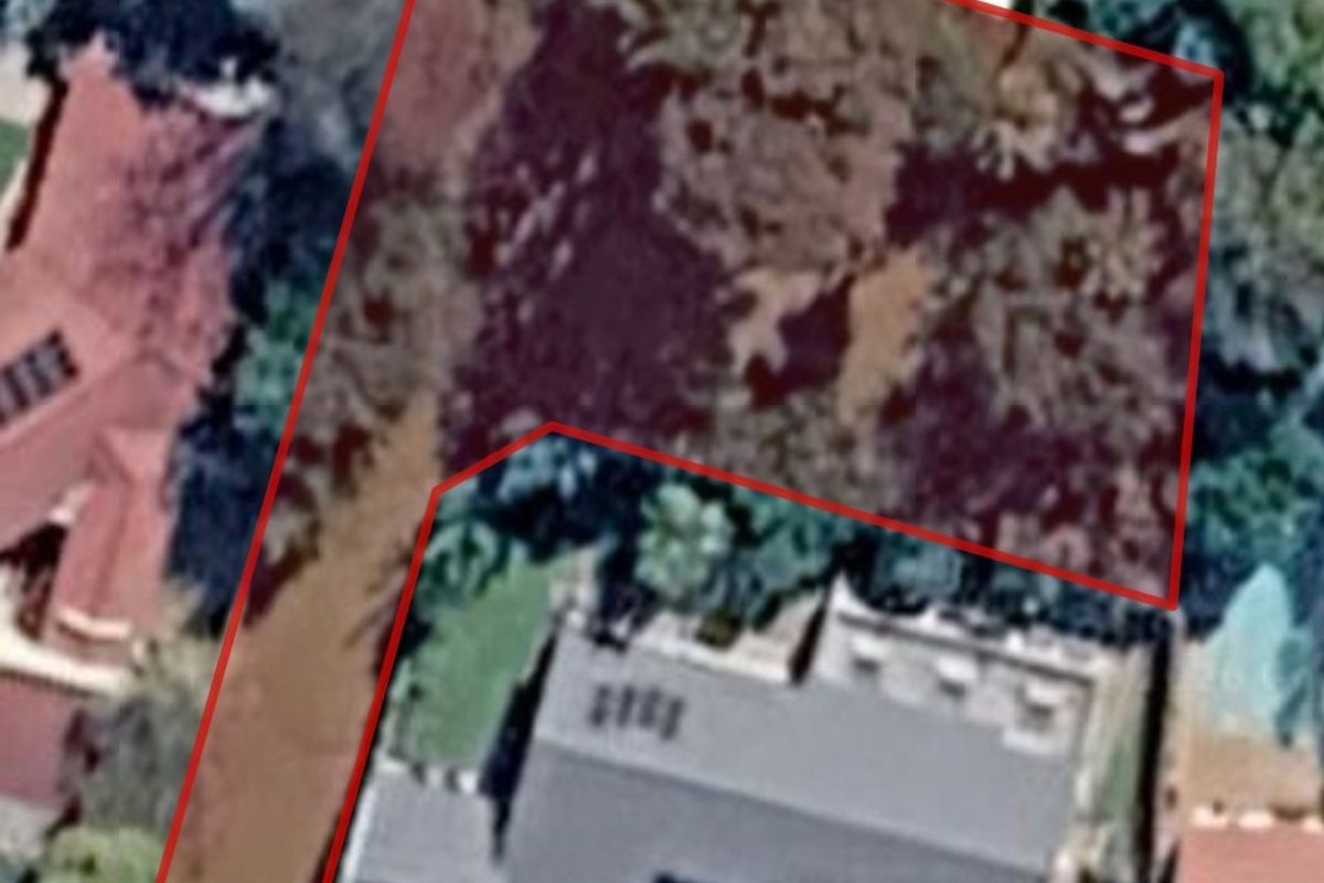 An aerial view of a vacant residential plot outlined in red, showing existing vegetation and proximity to neighboring properties.