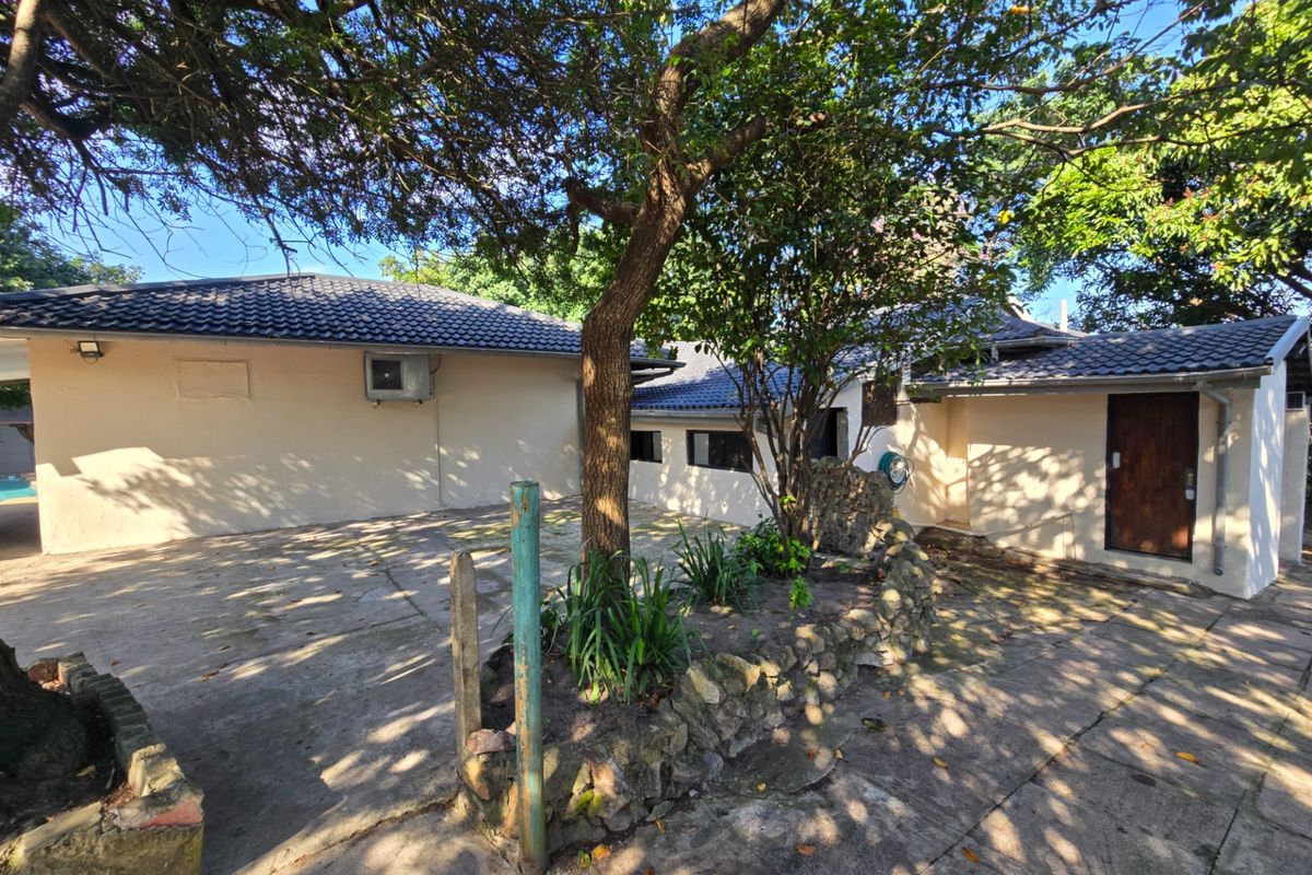Rear exterior view of the property featuring a concrete patio area, stone retaining wall, and mature trees.