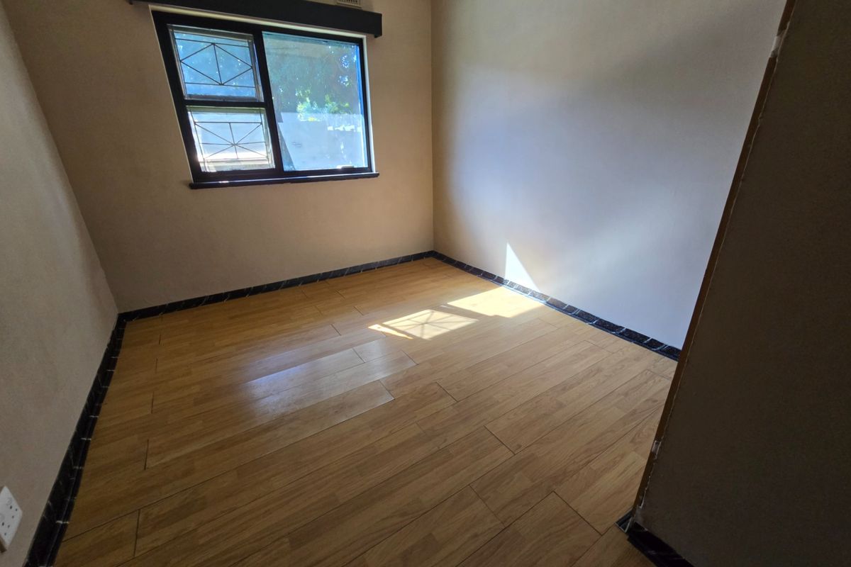 An empty bedroom featuring laminate wood-look flooring, a window with security bars, and dark skirting boards.