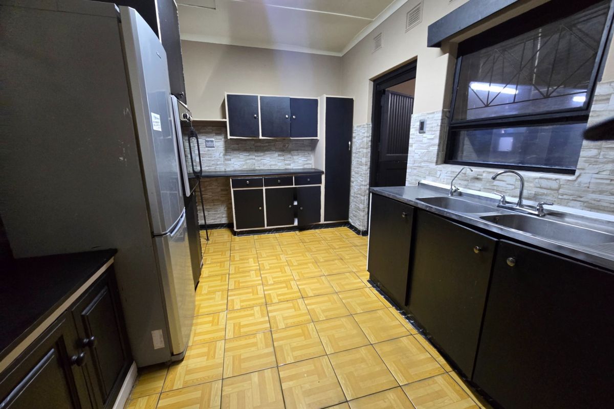 A functional kitchen featuring dark cabinetry, a double stainless steel sink, and tiled flooring, offering potential for a modern renovation.