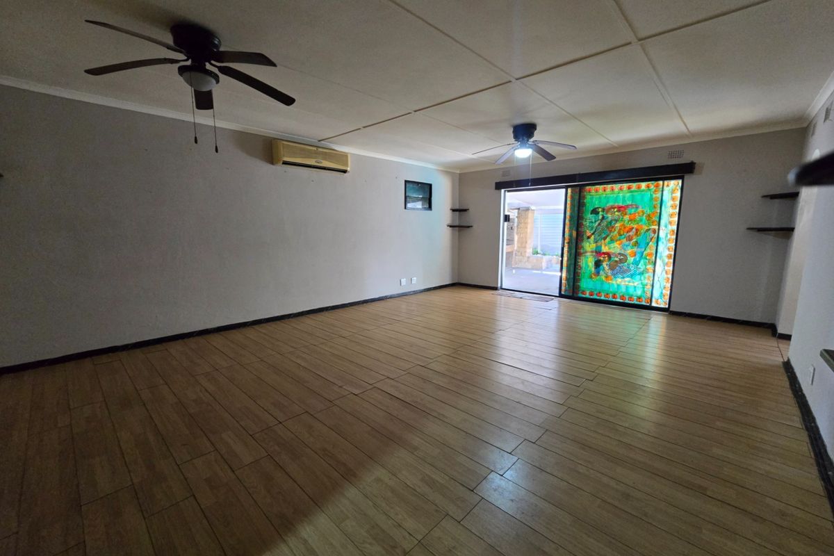 Spacious, empty living room featuring wood-look tile flooring, dual ceiling fans, a wall-mounted air conditioner, and sliding glass doors leading to the patio.