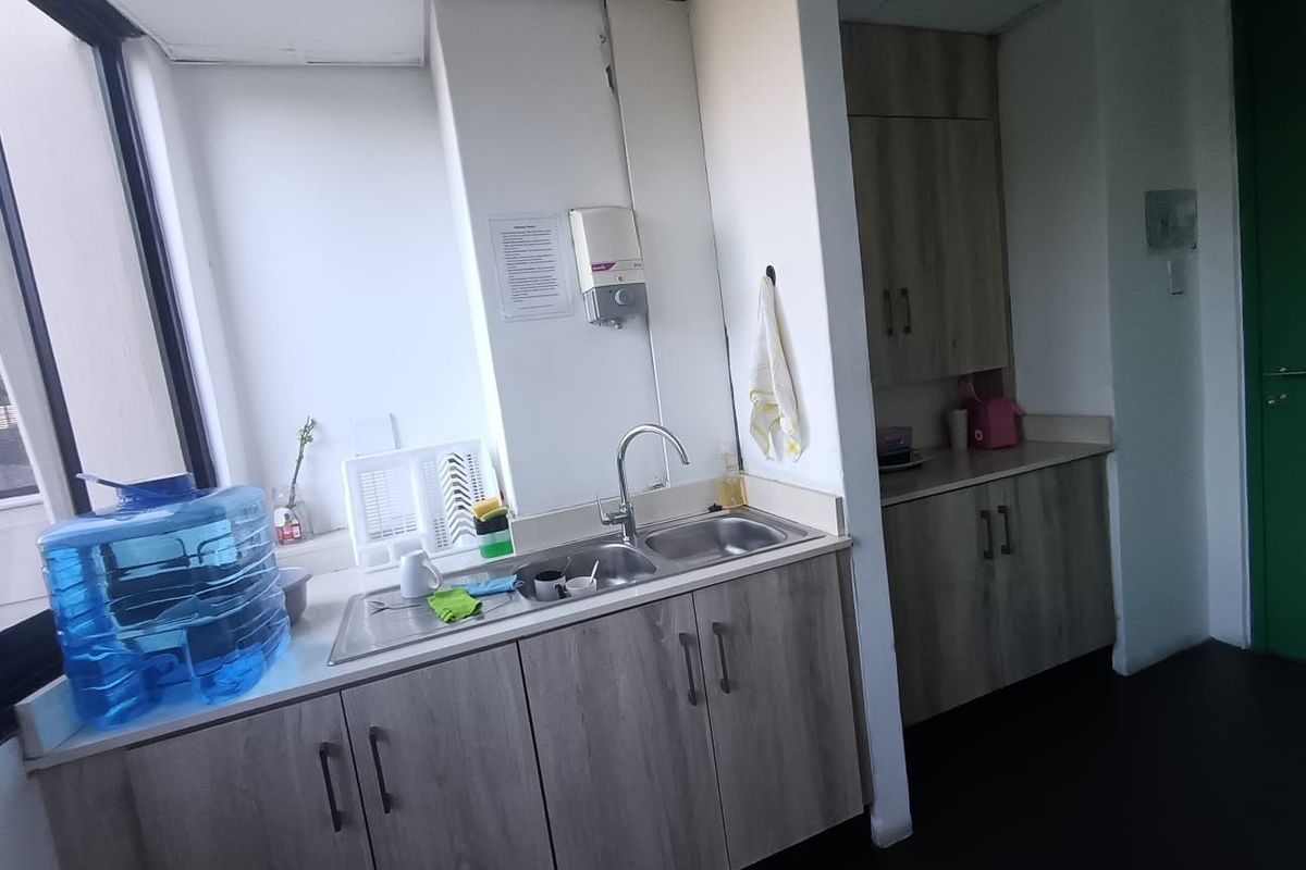 A functional office kitchenette featuring wood-grain cabinetry, a stainless steel double sink, and ample counter space for staff use.