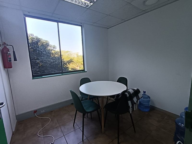 A functional office space featuring tiled flooring, a large window providing natural light, and a wall-mounted fire extinguisher.