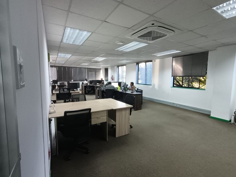 Open-plan office space featuring suspended ceiling tiles, recessed lighting, integrated air conditioning unit, and large windows with fitted blinds.