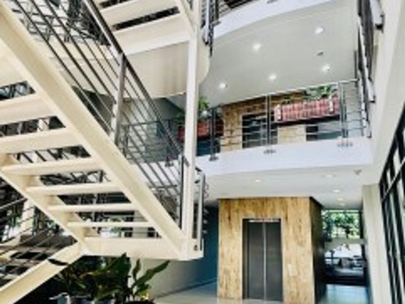Modern office building atrium featuring a prominent open staircase, glass and metal railings, and a central elevator with decorative stone-look cladding.