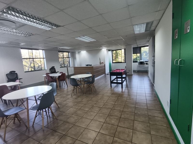 Spacious open-plan office area featuring tiled flooring, recessed fluorescent lighting, and large windows providing ample natural light.