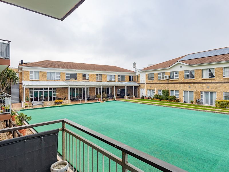 View of a well-maintained communal bowling green within a retirement village complex, featuring surrounding residential units with balconies and covered patios.