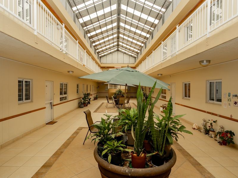 A bright, covered atrium area within the retirement village, featuring a large skylight, tiled flooring, and access to multiple residential units.