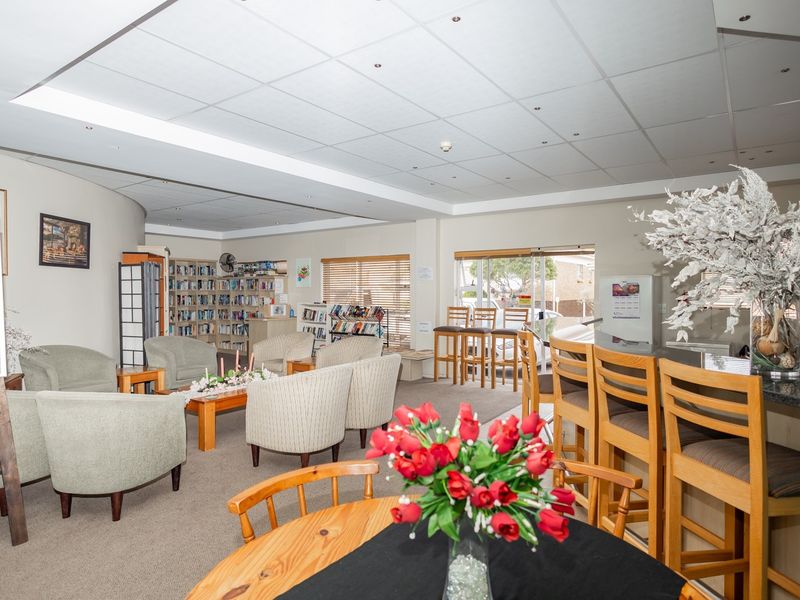 A spacious communal clubhouse area featuring a built-in bar counter, integrated shelving for a library, and comfortable seating arrangements for residents.