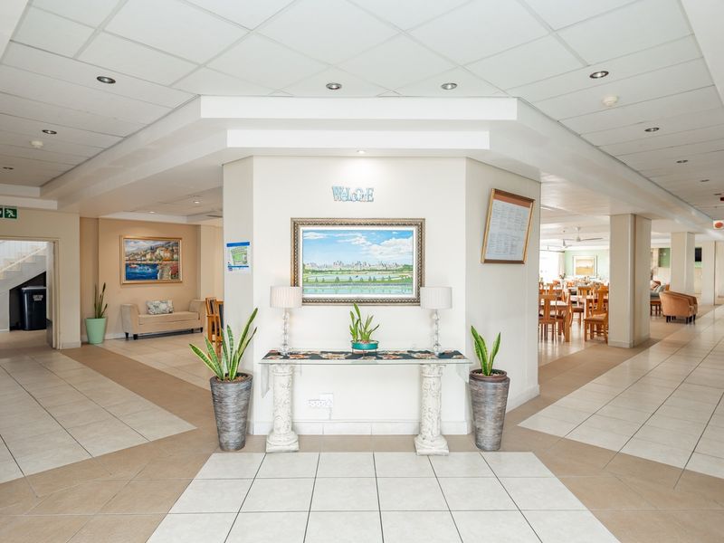 Spacious retirement village entrance foyer featuring tiled flooring, recessed lighting, and a central reception area leading to communal dining and circulation spaces.
