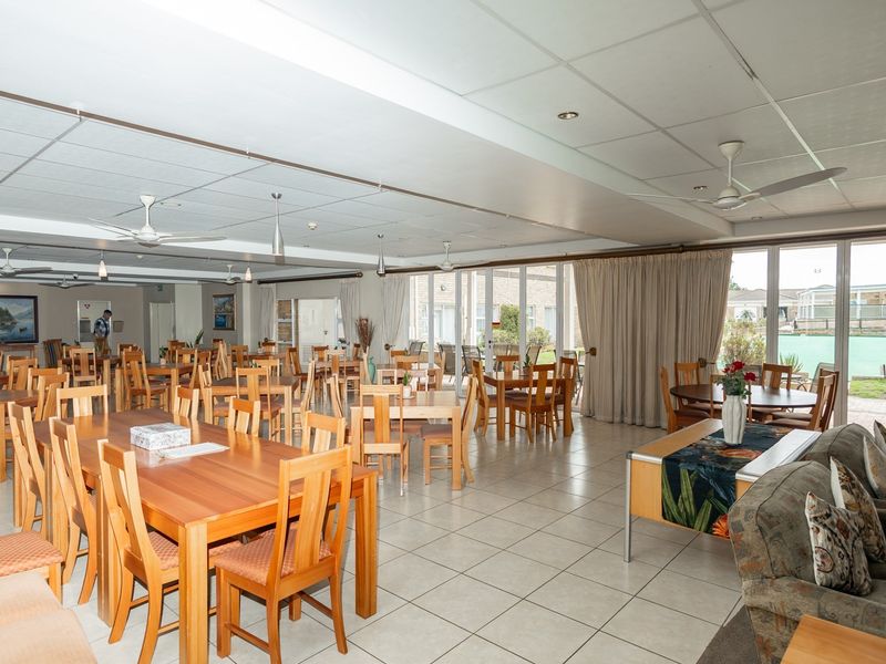 Spacious communal dining and lounge area in a retirement village, featuring tiled floors, ceiling fans, and large sliding doors opening to an outdoor area.