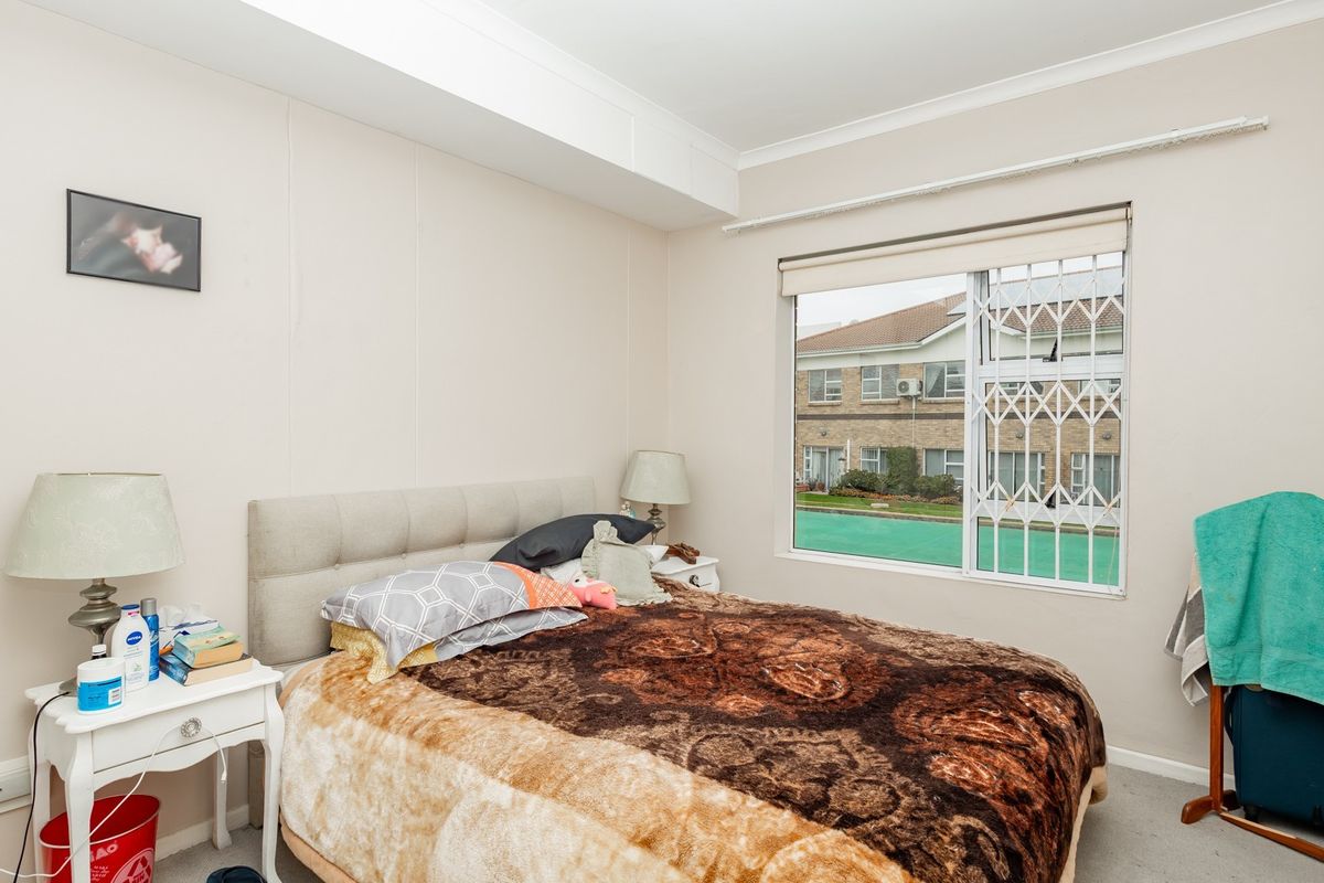 A functional bedroom featuring a sliding window with a security gate, neutral wall finishes, and coving detail.