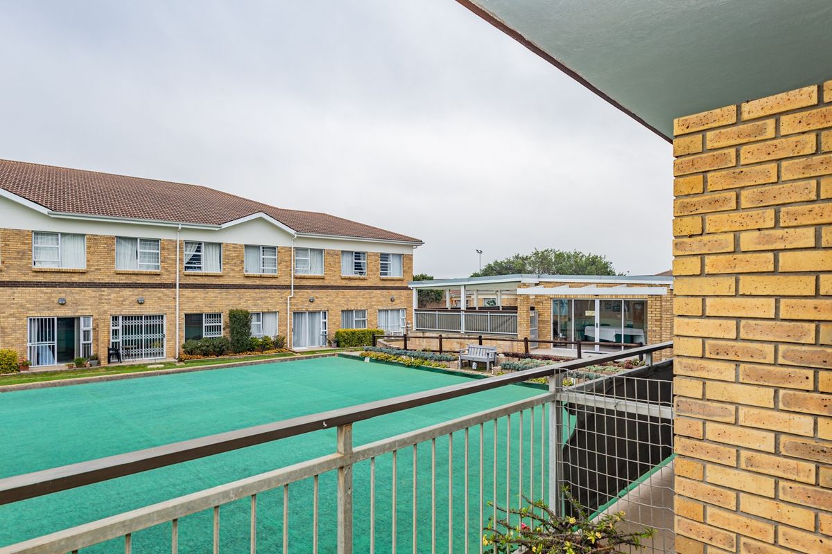 View from a balcony overlooking a communal courtyard area with artificial lawn and surrounding brick retirement village residential buildings.