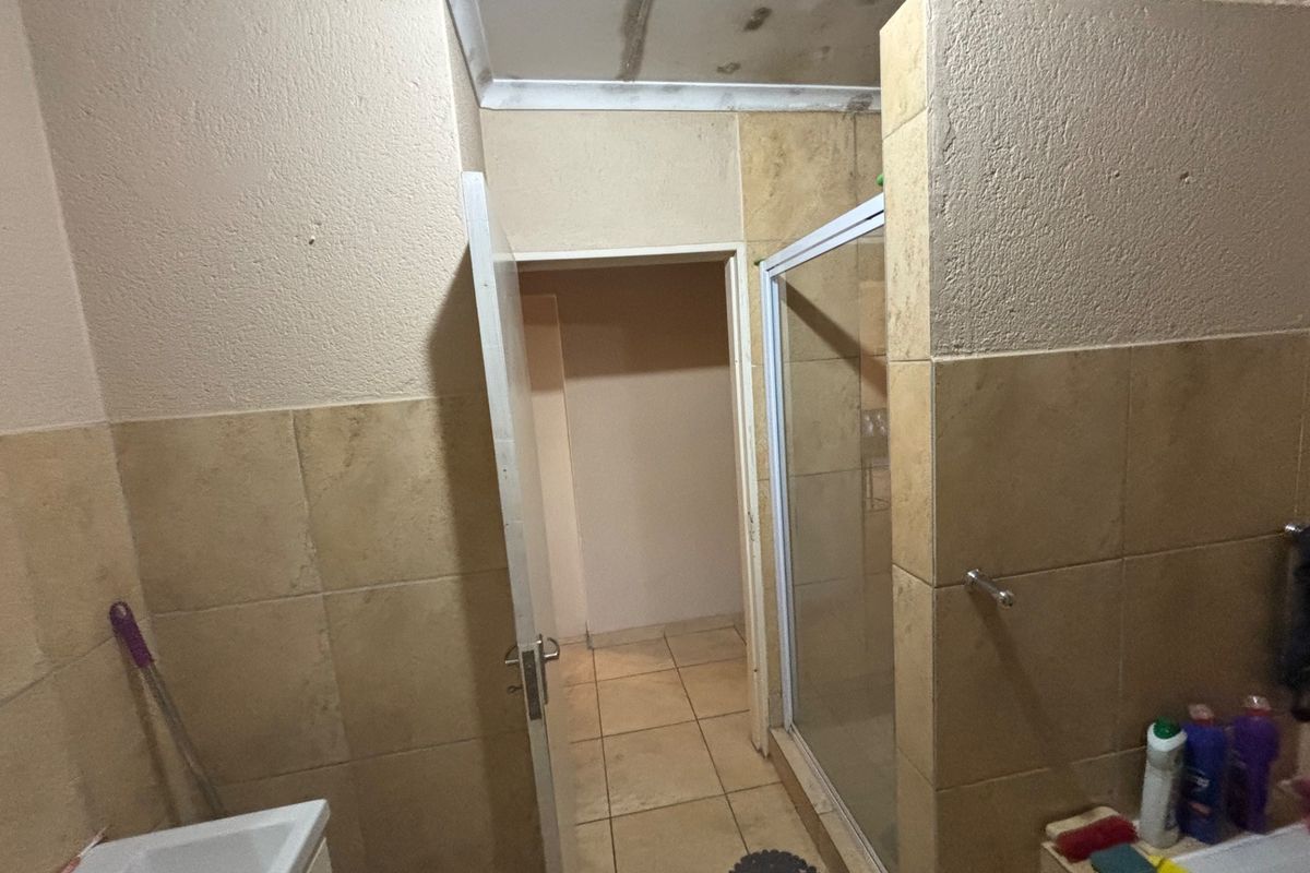A bathroom featuring a tiled shower enclosure and neutral wall finishes, showing signs of ceiling water damage and general wear.