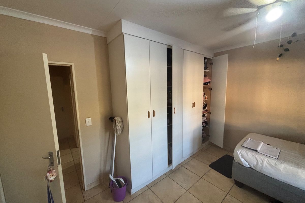 A bedroom featuring built-in floor-to-ceiling wardrobes, tiled flooring, and a ceiling fan, providing functional storage and living space.
