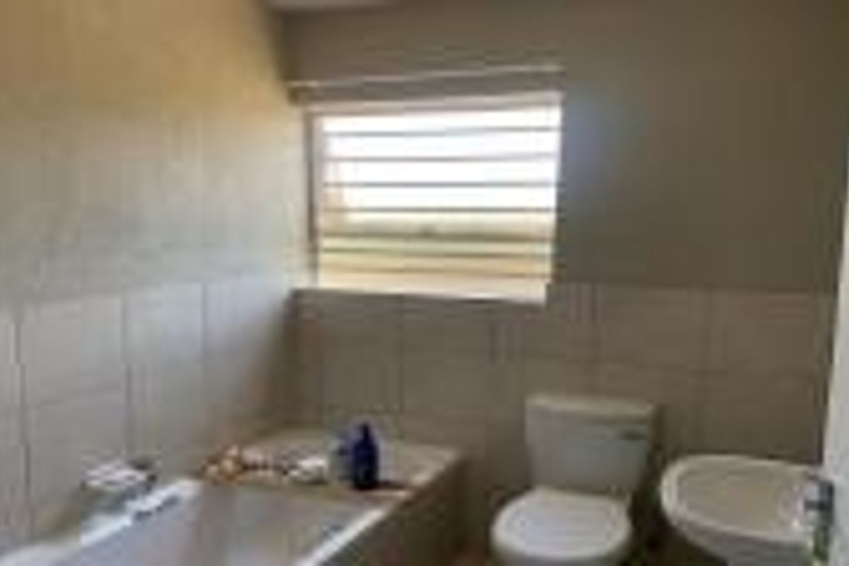 A functional bathroom featuring a built-in bathtub, a standard toilet, and a wall-mounted basin with tiled splashbacks and a window with horizontal blinds.