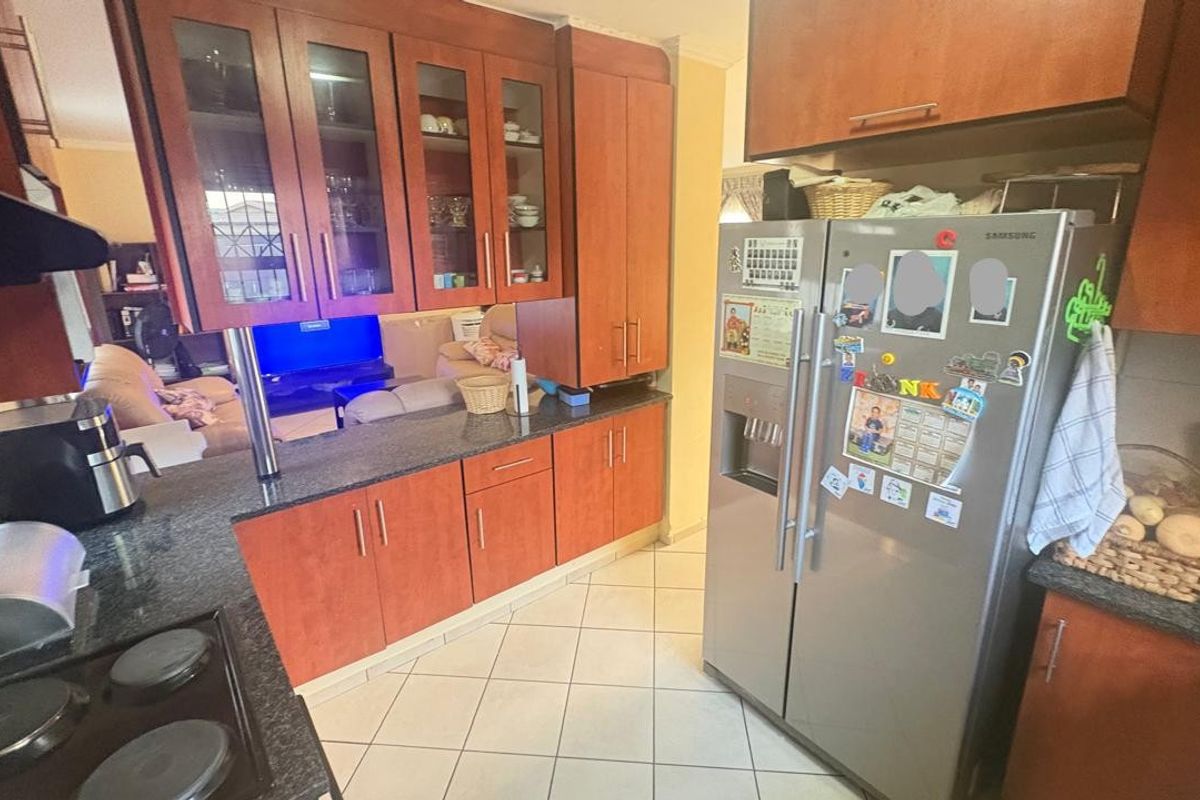A functional kitchen featuring wood-finish cabinetry, granite countertops, and a tiled floor, with an open-plan layout connecting to the adjacent living area.