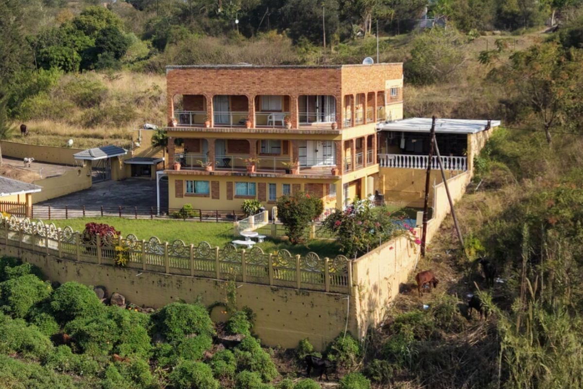 Aerial view of a three-story brick residential property featuring multiple balconies, a perimeter wall, and a driveway, set within a rural landscape.