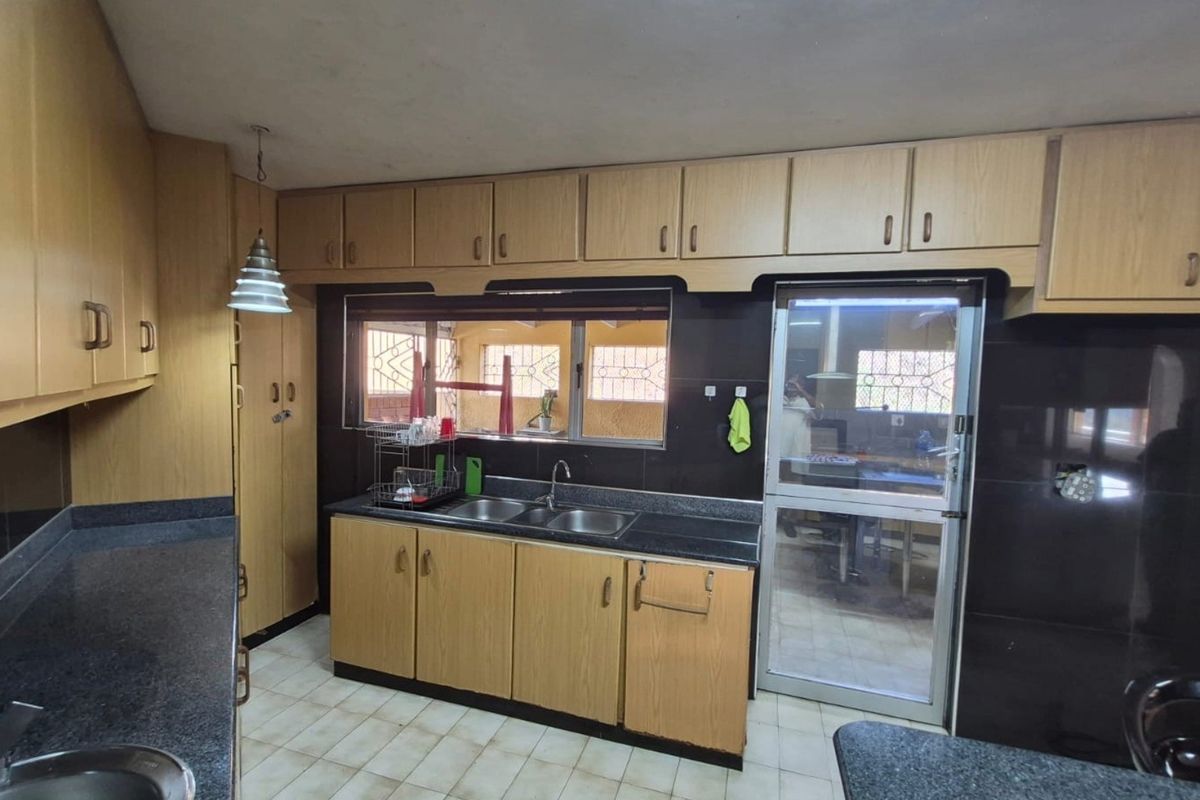 A functional kitchen featuring laminate cabinetry, granite countertops, a double bowl sink, and a tiled backsplash with direct access to an adjacent area.