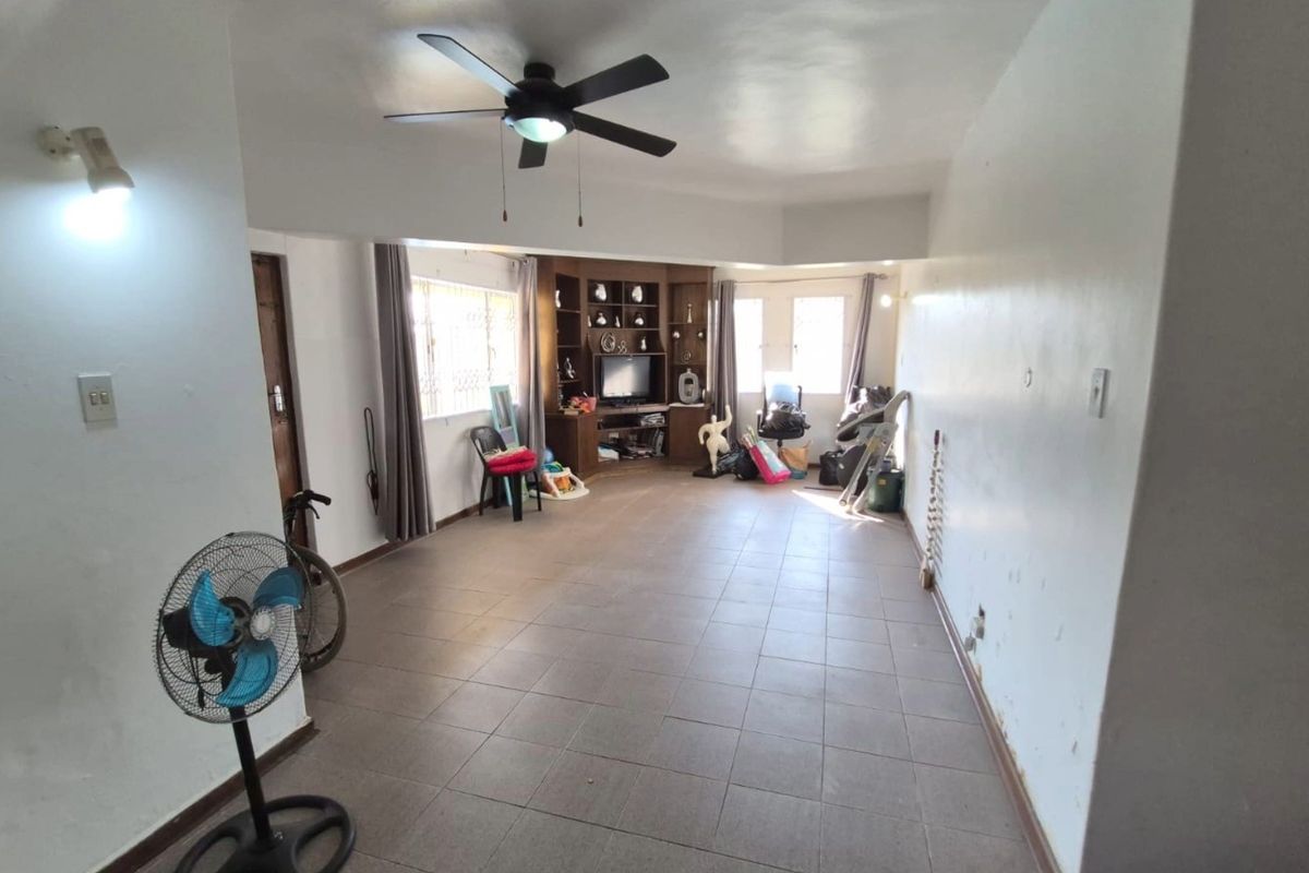 Spacious living area featuring tiled flooring, a ceiling fan, and a built-in wooden shelving unit, offering a versatile layout for comfortable family living.
