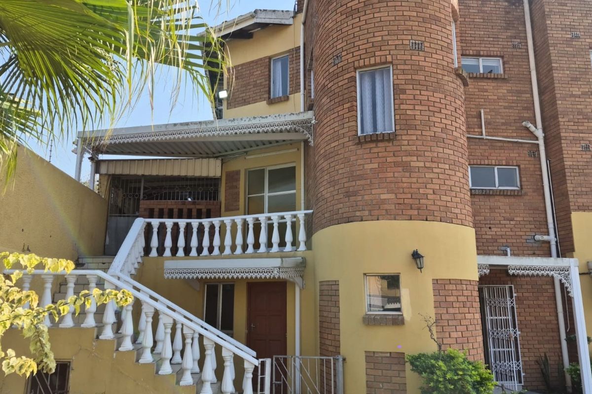 Rear elevation of a multi-story brick townhouse featuring a prominent circular architectural element, external staircase, and a balcony with decorative balustrades.