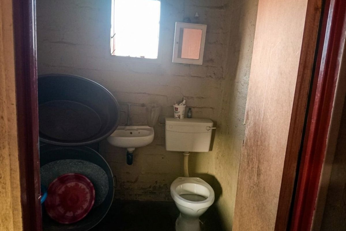 A small, basic bathroom featuring a standard toilet, wall-mounted basin, and a small window, requiring significant renovation and cosmetic updates.