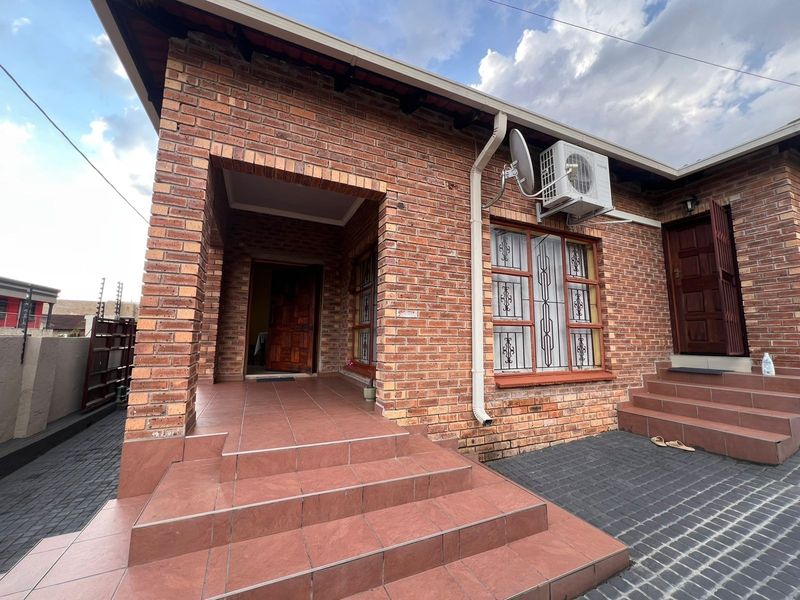 Front exterior view of a face brick house featuring a covered entrance porch, tiled steps, and paved driveway area.