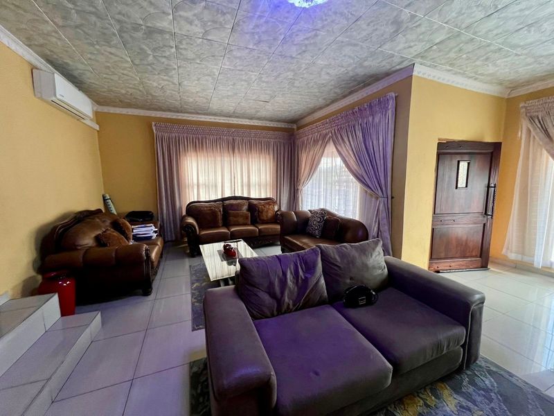 A spacious living room featuring tiled flooring, a split-system air conditioner, and textured ceiling tiles, offering a functional layout for family relaxation.