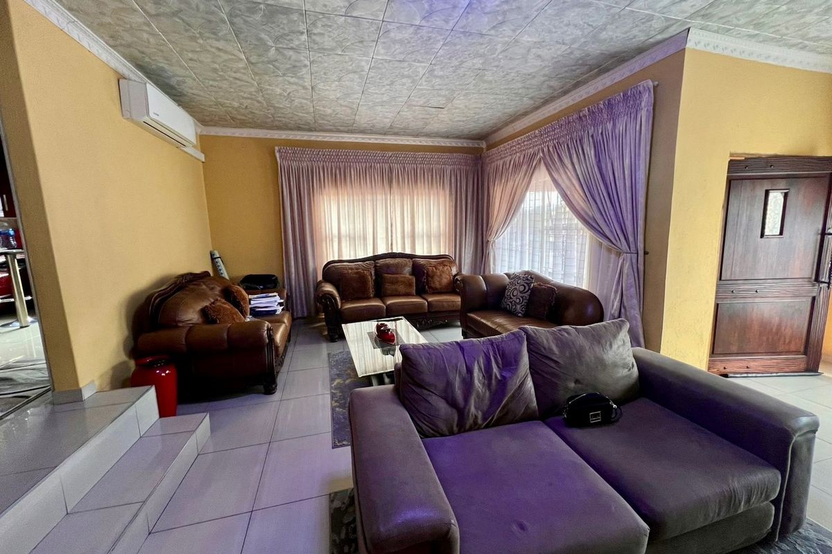 Spacious living room featuring tiled flooring, decorative ceiling tiles, and a wall-mounted air conditioning unit, offering a comfortable and functional living space.