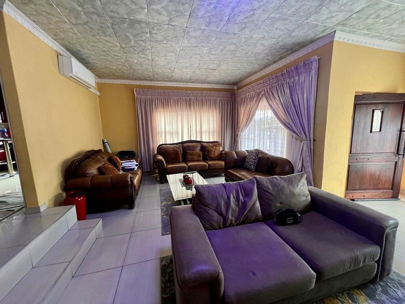 Spacious living room featuring tiled flooring, decorative ceiling tiles, and a wall-mounted air conditioning unit, offering a comfortable and functional living space.